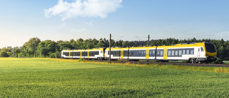 Gelbe Regionalbahn fährt an Wiese entlang