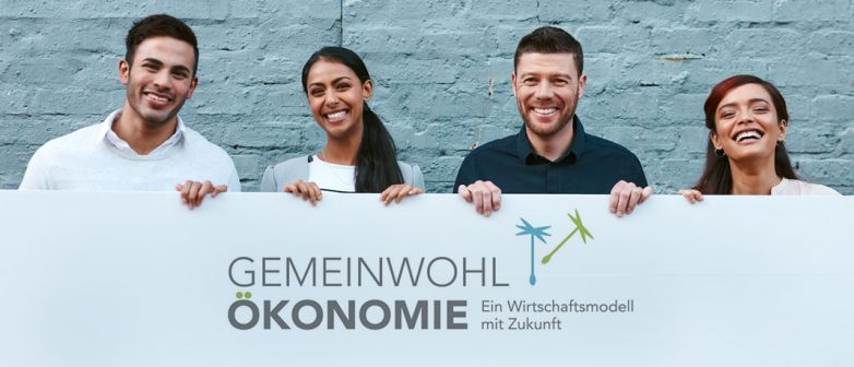 Drei Personen zeigen ein Transparent mit dem Gemeinwohl-Ökonomie-Logo.